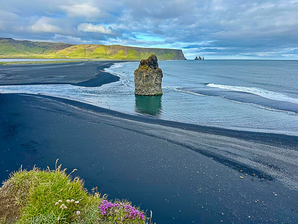 Schwarzer Strand mit einem Felsen im Meer