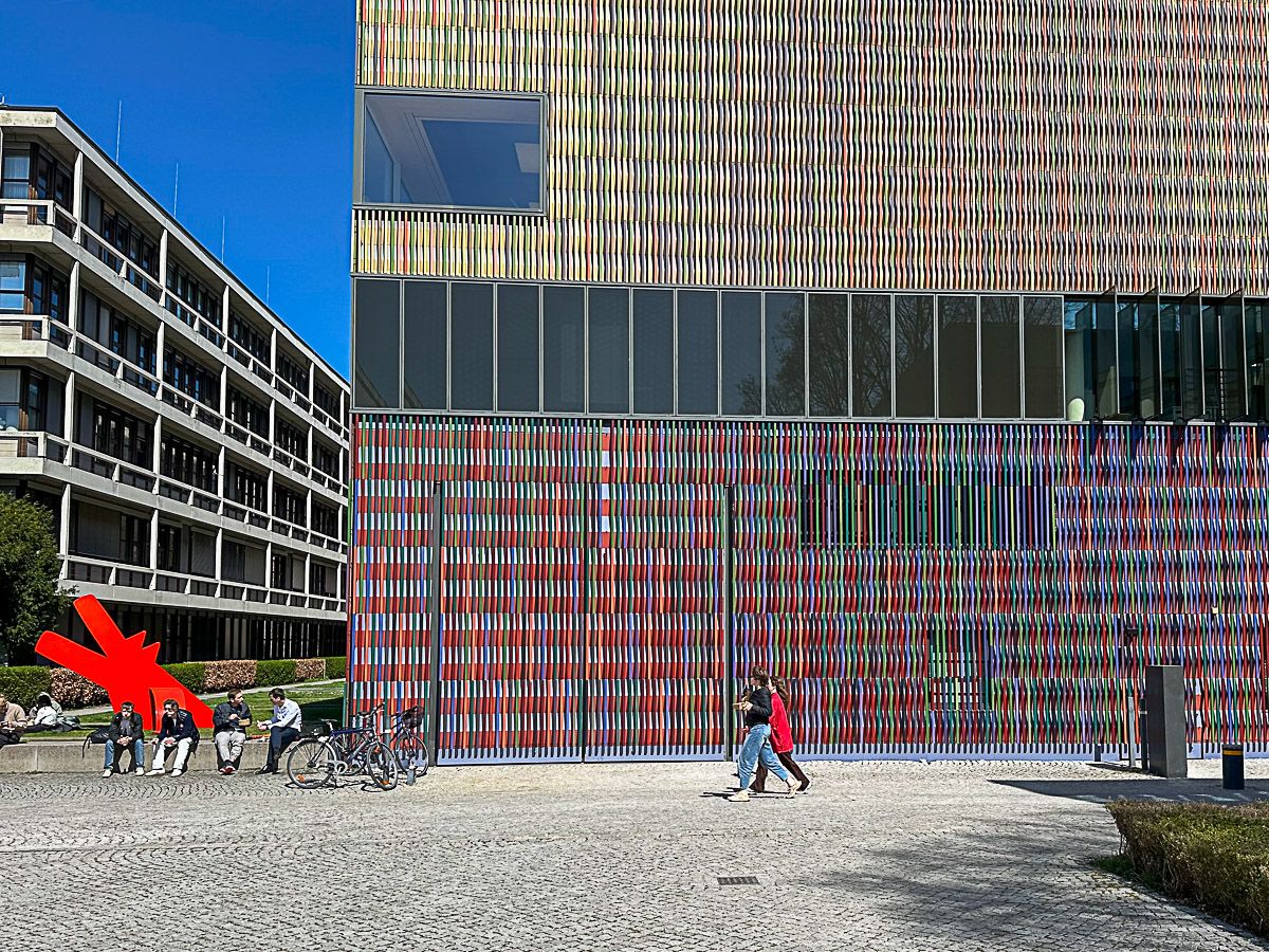 Ein Museumsbau mit farbigen Keramikbändern an der Fassade. Davor genießen Menschen die Sonne. 