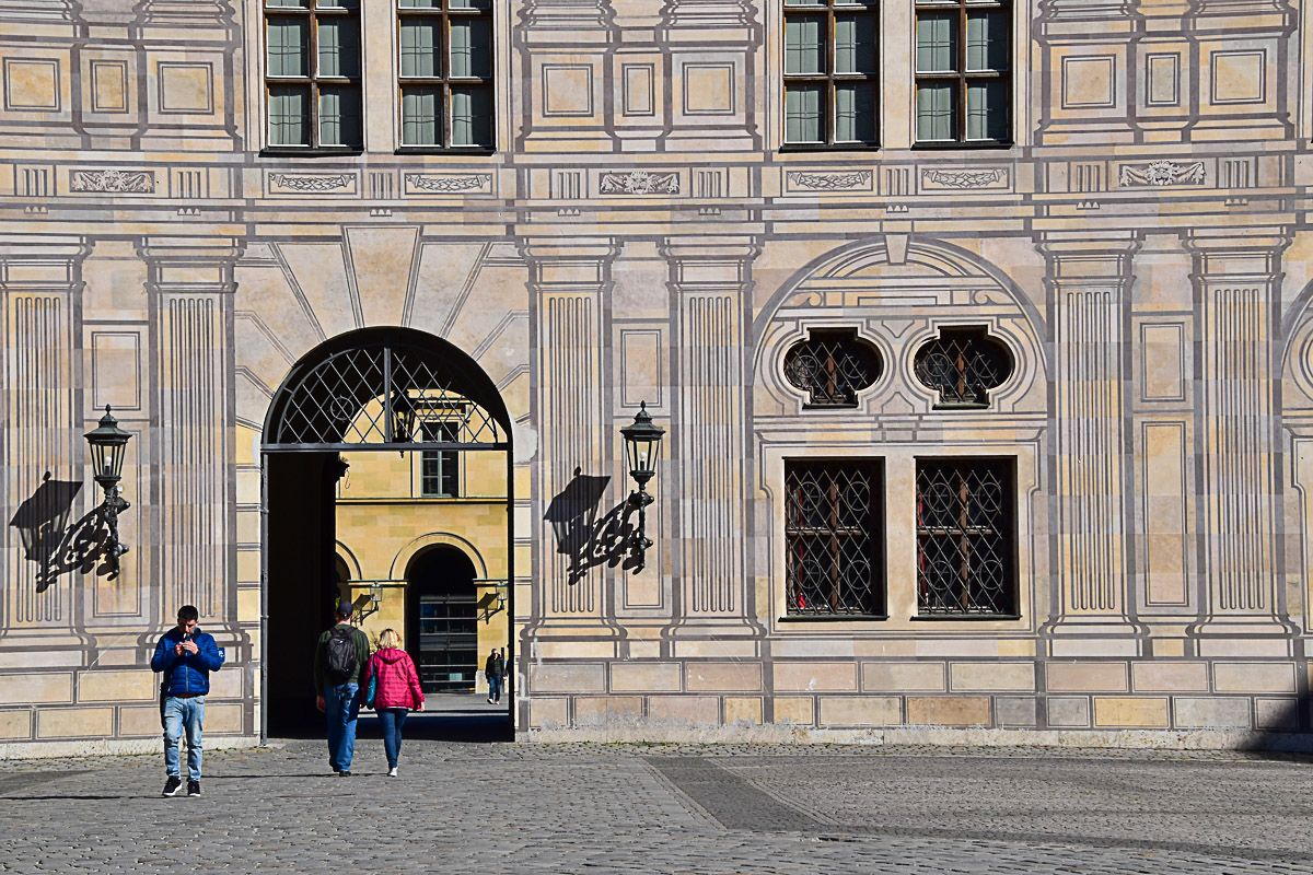 Drei Menschen spazieren durch einen der Höfe der Residenz mit illusionistischer Malerei.