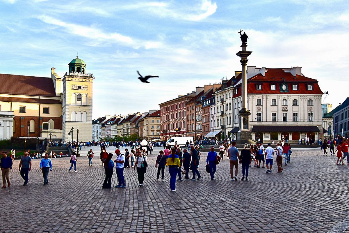 Menschen auf einem  Marktplatz mit einer Säule und historischen Häusern ringsum