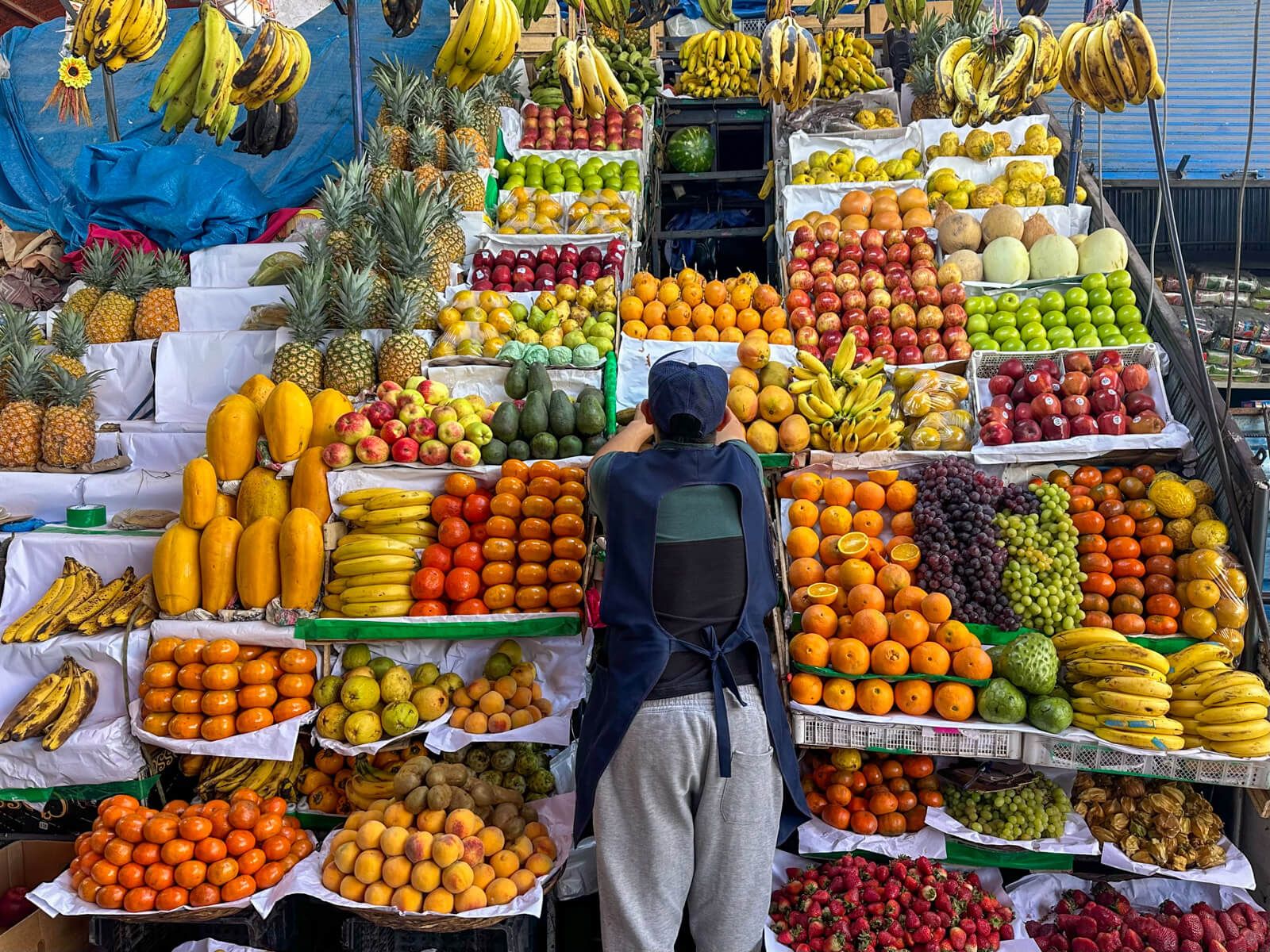 Mann steht vor einem riesigen Obststand auf dem Markt