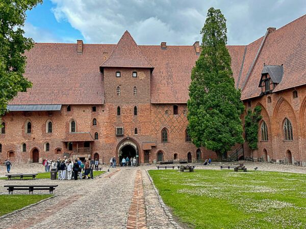 Tagesausflüge ab Danzig: Der Innenhof der Marienburg in Malbork: Gebäude aus roten Backstein und Grünflüche, wo sich Besucher sammeln