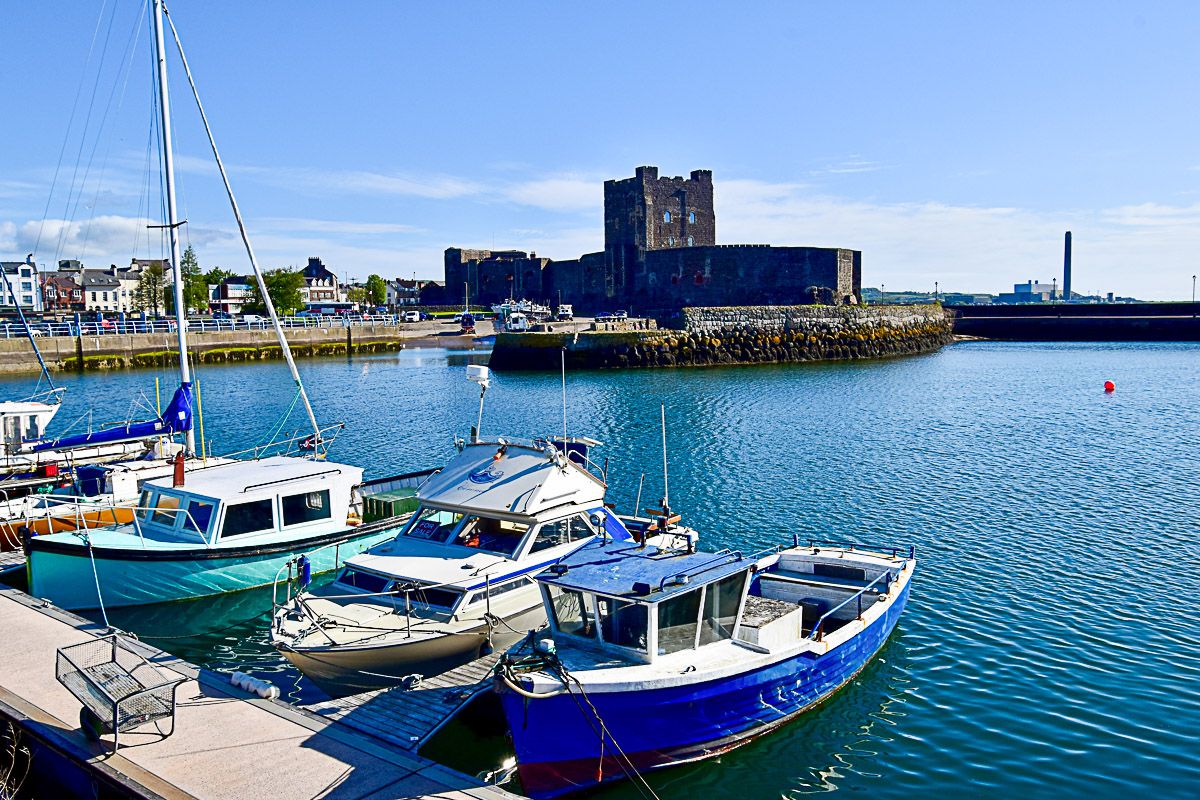 Roadtrip Nordirland: ein Hafen mit ein paar kleinen Booten, dahinter die Normannenburg Carrckfergus