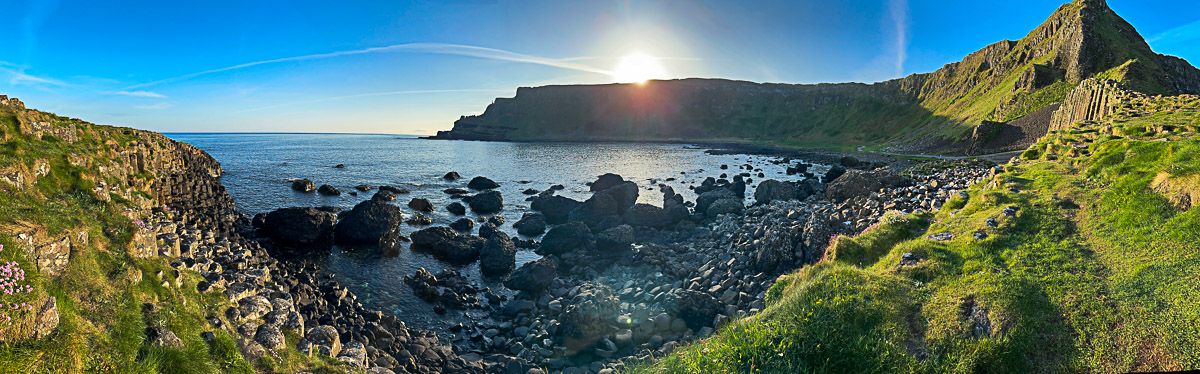 Panorama mit schwarzen Basaltäsulen und grünen Hügeln vor dem Meer