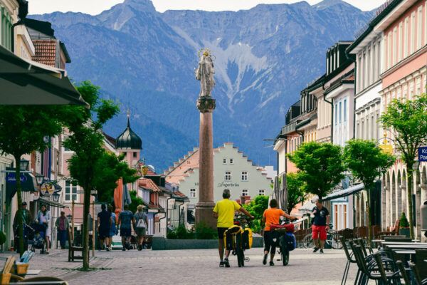 10 traumhafte Radtouren in Oberbayern zwischen München und Berchtesgaden 3 Radtouren in Oberbayern: Fahrradfahrer schieben durch Murnau. Im Hintergrund die Alpen.