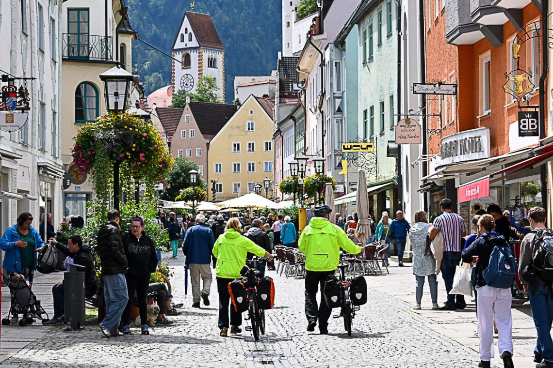 Menschen drängen sich in der Haupteinkaufsstraße von Füssen. Im Hintergrund das Hohe Schloss.