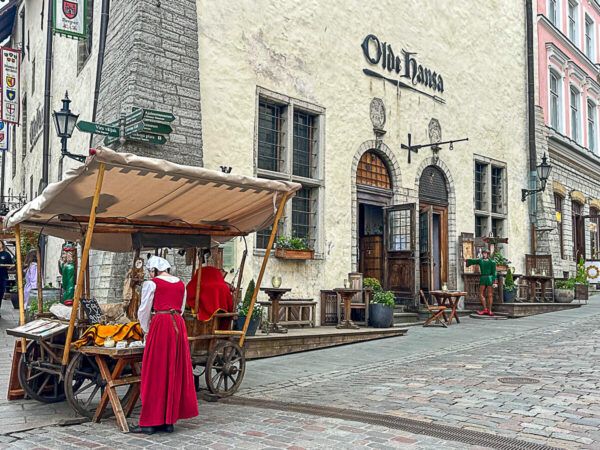 Roadtrip Estland 1 Woche: Ostseeküste, Moore und eine coole Hauptstadt 18 Das Mittelalterrestaurant Olde Hanse in Tallinn. Davor ein Marktstand mit einer Frau in mittelalterlicher Kleidung.