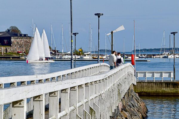 Eine coole nordische Schönheit: 3 Tage Helsinki – Reisetipps für deinen Städtetrip 60 Weißer Steg, der ins Meer führt mit zwei Männer. Dahinter ein Jachthafen mit Segelschiffen