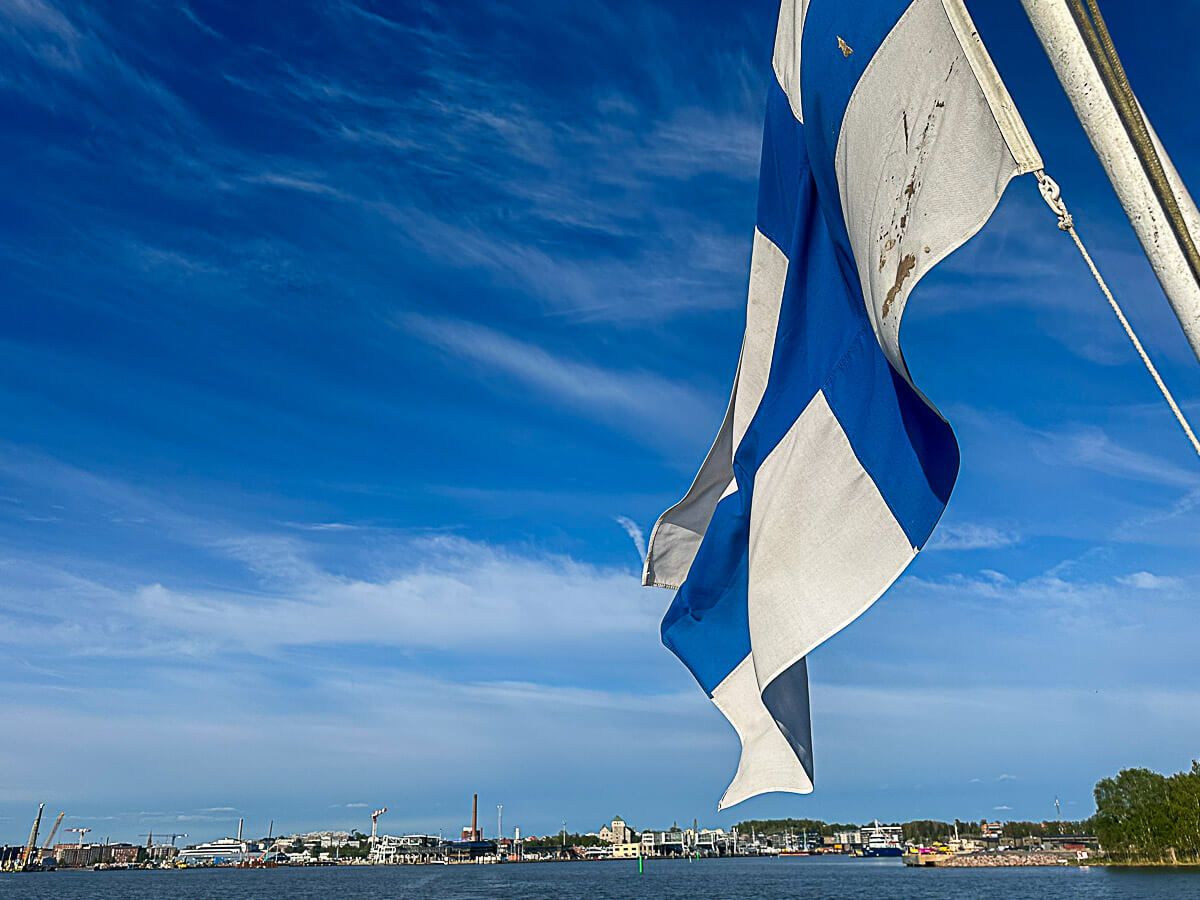Mit dem Zug durch Finnland: Helsinki – Turku – Tampere 51 Turku, Schärengarten: im Vordergrund die finnische Flagge, im Hintergrund der Hafen von Turku