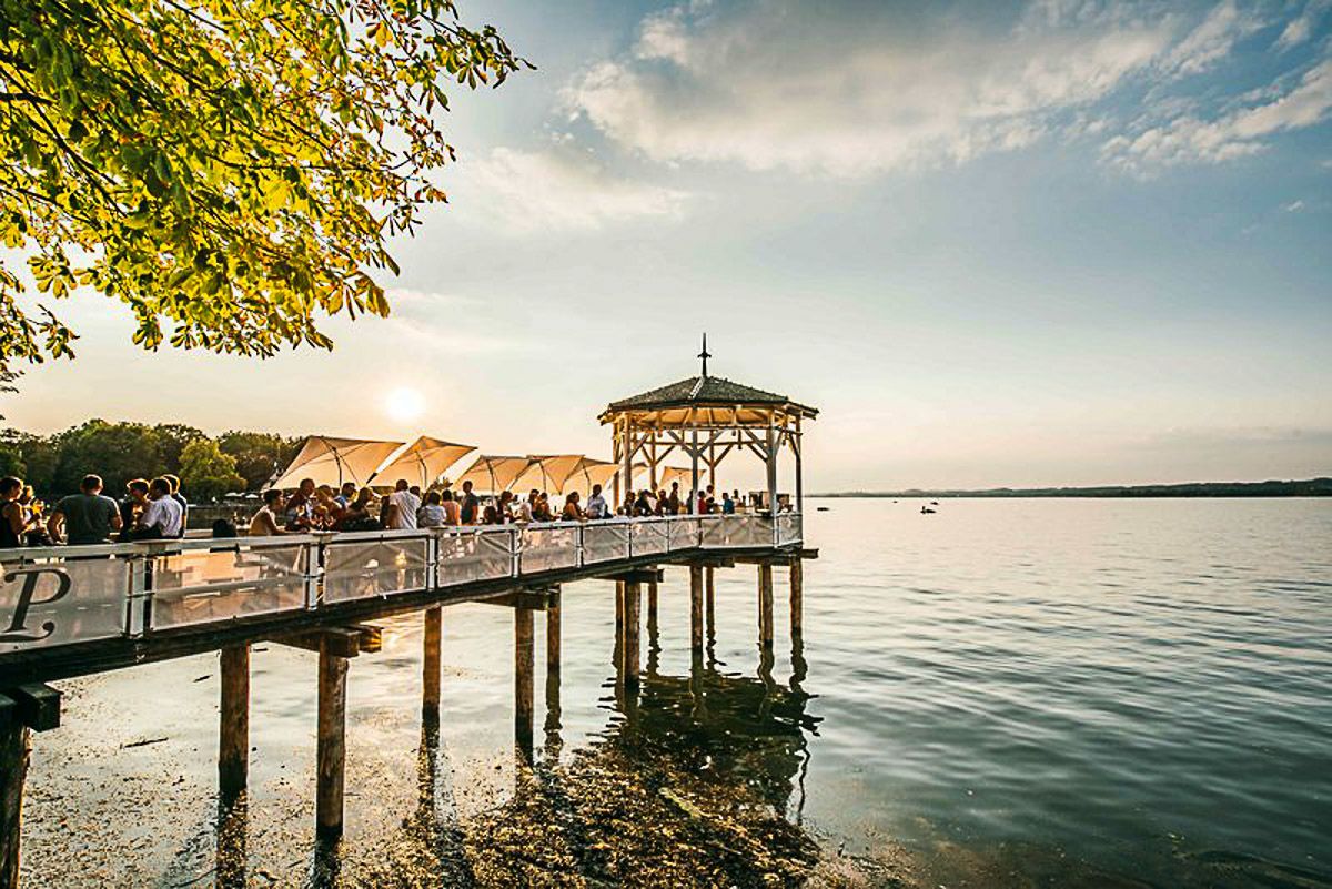 Steg mit hölzernem Pavillon bei Sonnenuntergang mit feiernden Menschen