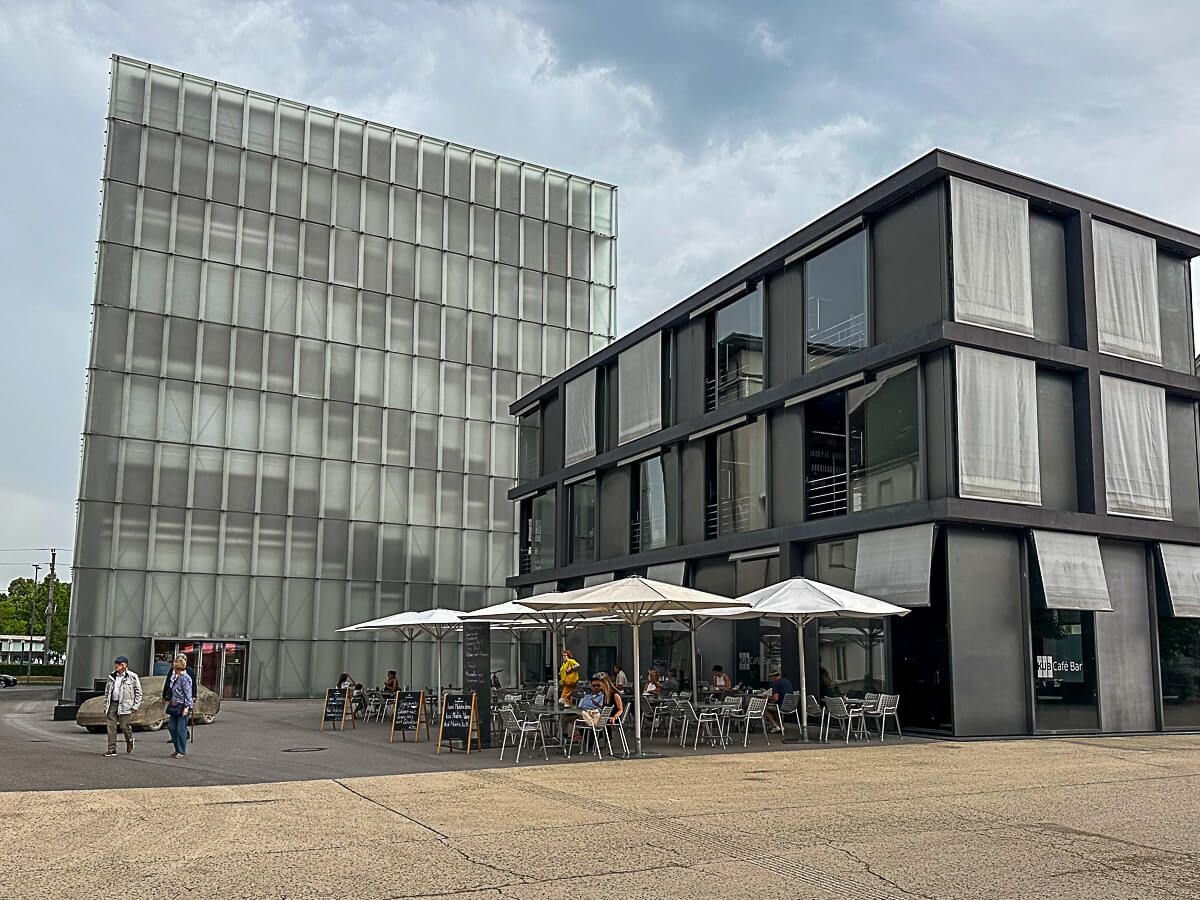 Museumsturm mit gläserner Fassade, davor ein Café