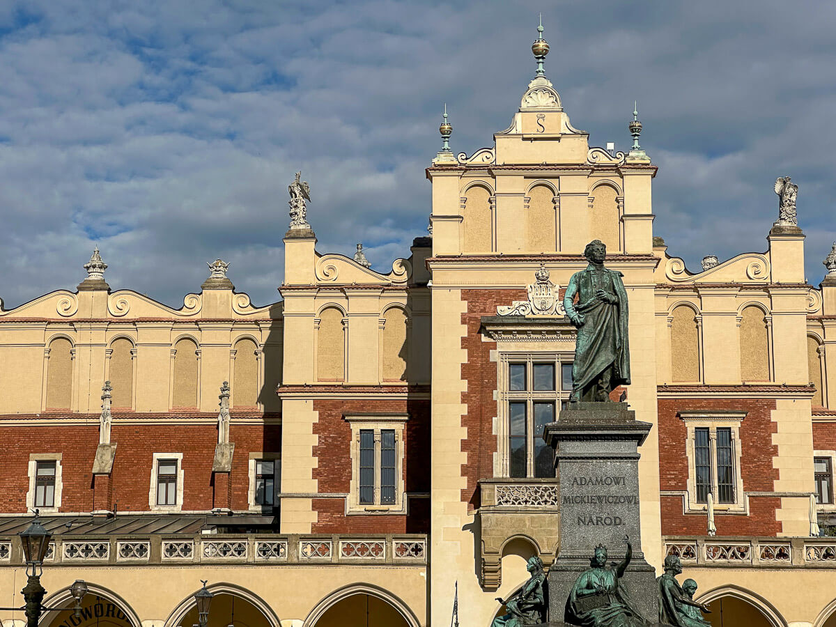 Renaissancegebäude in Creme und Rot und davor das Denkmal für den polnischen Nationaldichter