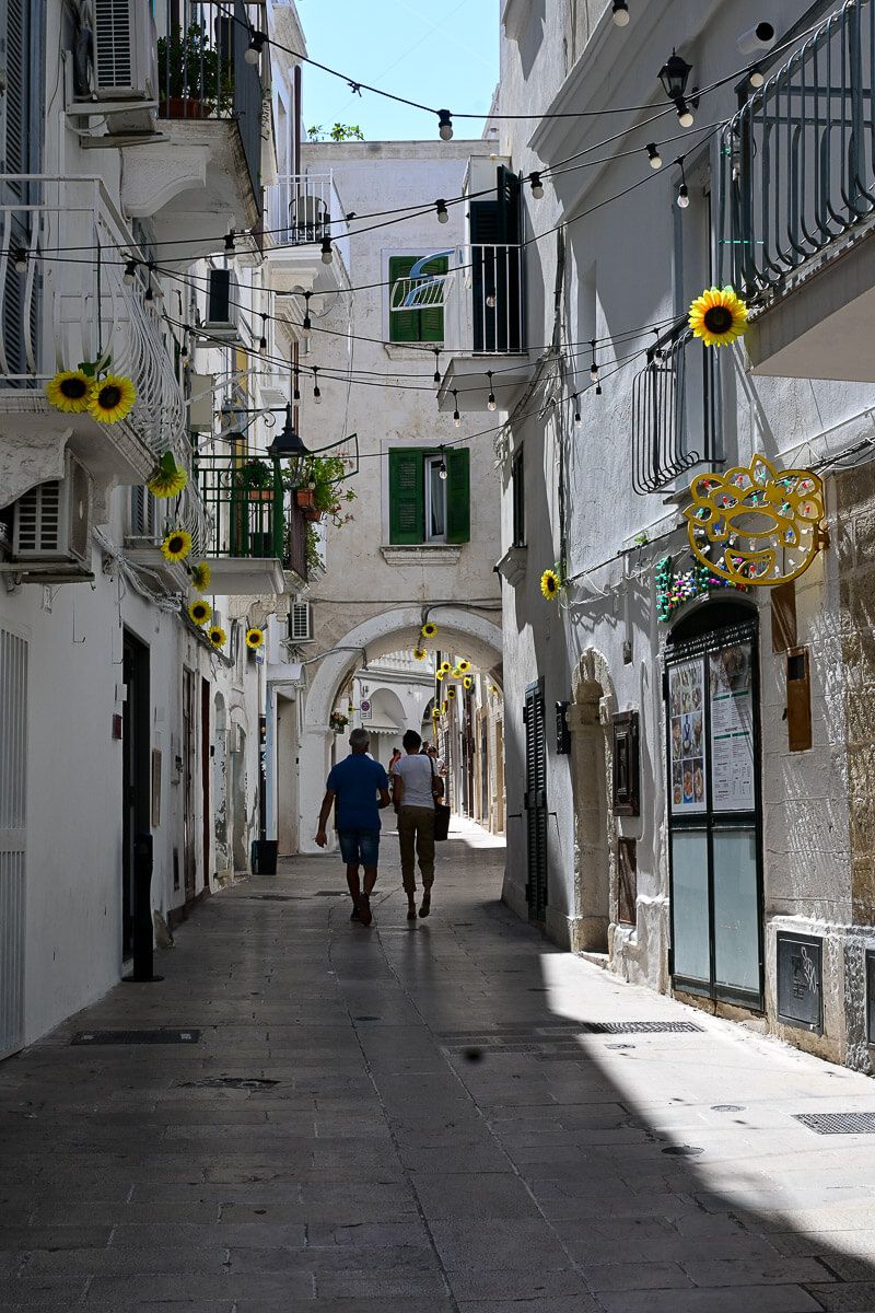 Gasse in Monopoli mit weißen Häusern, Sonnenblumen-Deko und Rundbogen