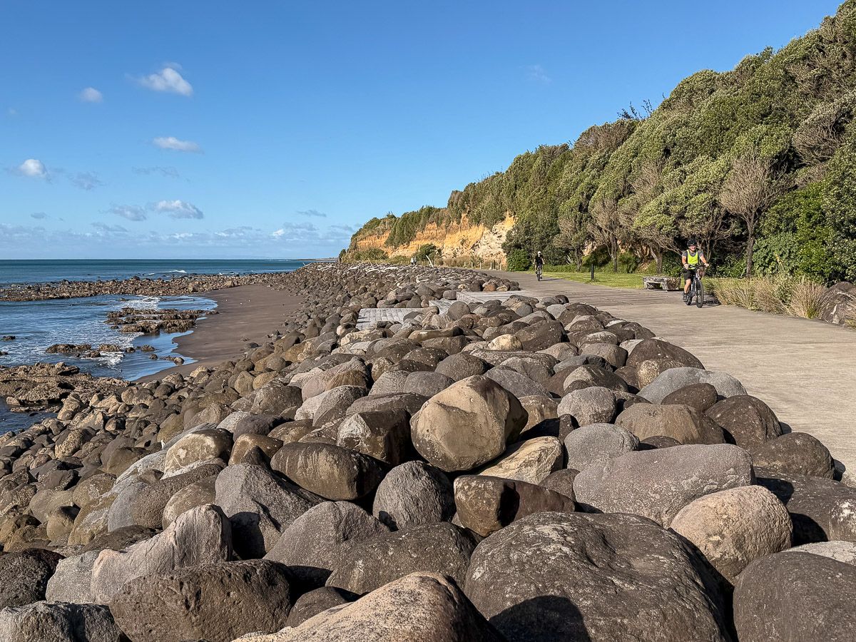 Neuseeland: Reisetipps für Mount Taranaki und New Plymouth 10 Reisetipps für New Plymouth: Radfahrer auf dem Coastal Walk Way, der direkt an einem schwarzen Strand mit vielen Steinen vorbeiführt