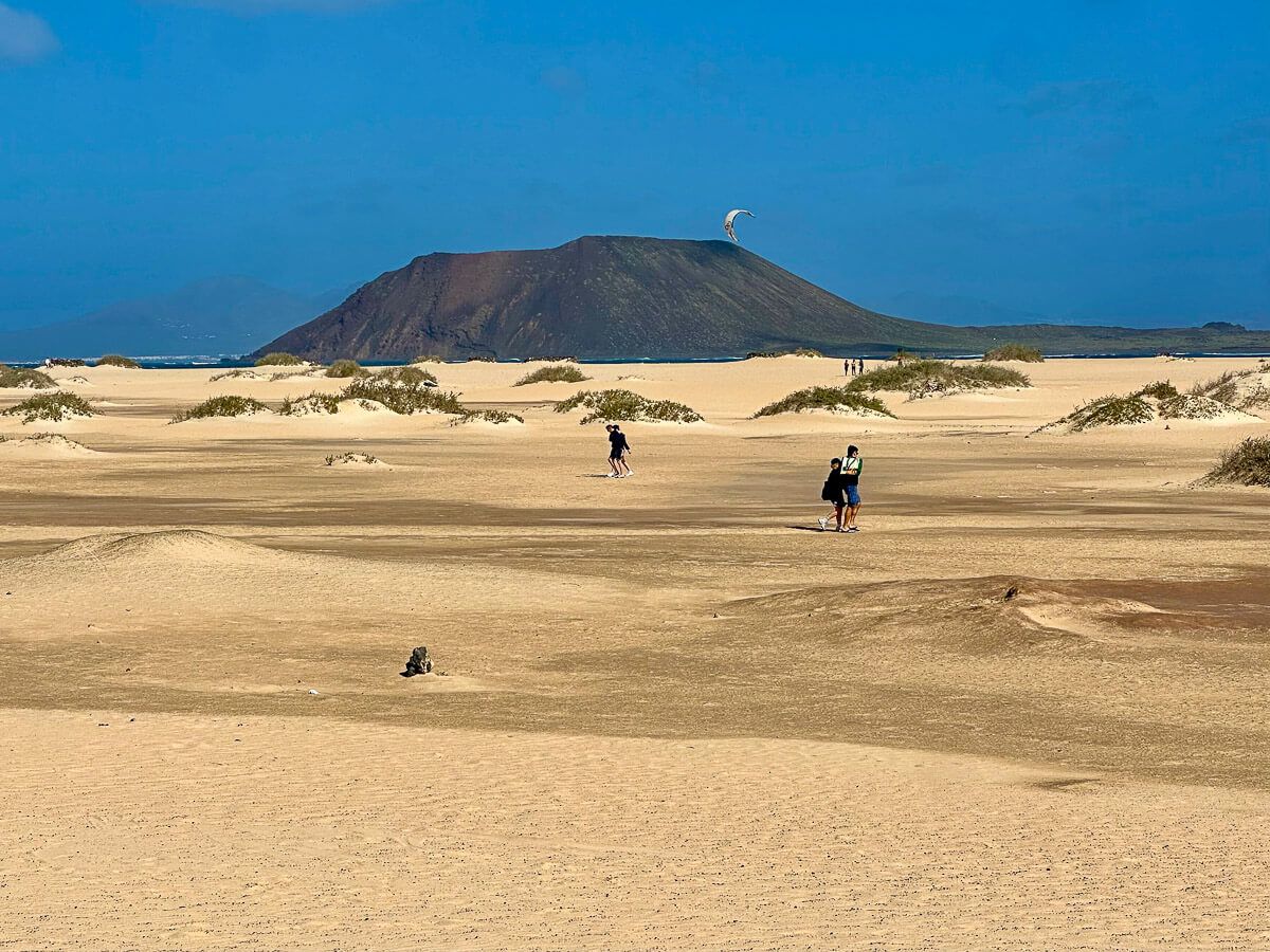 Reisetipps Fuerteventura: Düne am Meer mit wenigen Spaziergängern; im Hintergrund ein Hügel