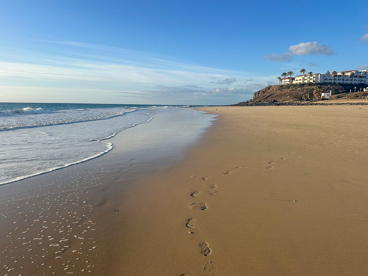 langer Strand, im Hintergrund ein Hotel in erhöhter Lage