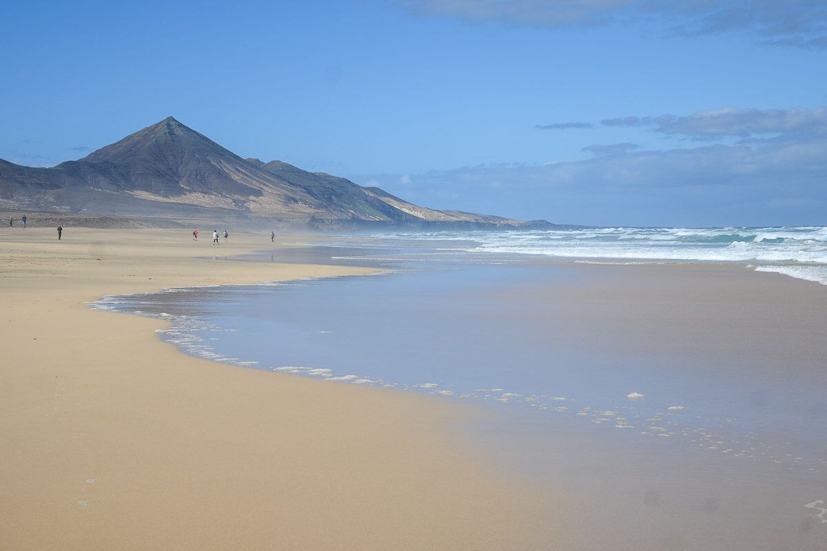 wilder Strand mit wenigen Spaziergängern und einer Bergspitze im Hintergrund 