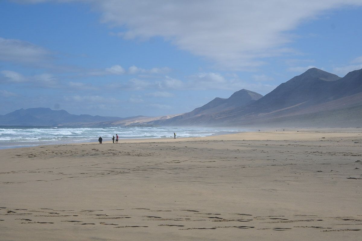 wilder Strand mit wenigen Spaziergängern und einer Bergspitzen im Hintergrund