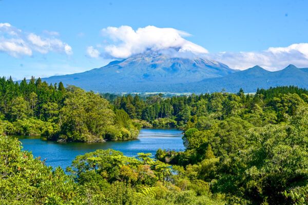 Vulkangipfel umgeben von Wolken vor der Kulisse eines Sees mit Baumfarnenb