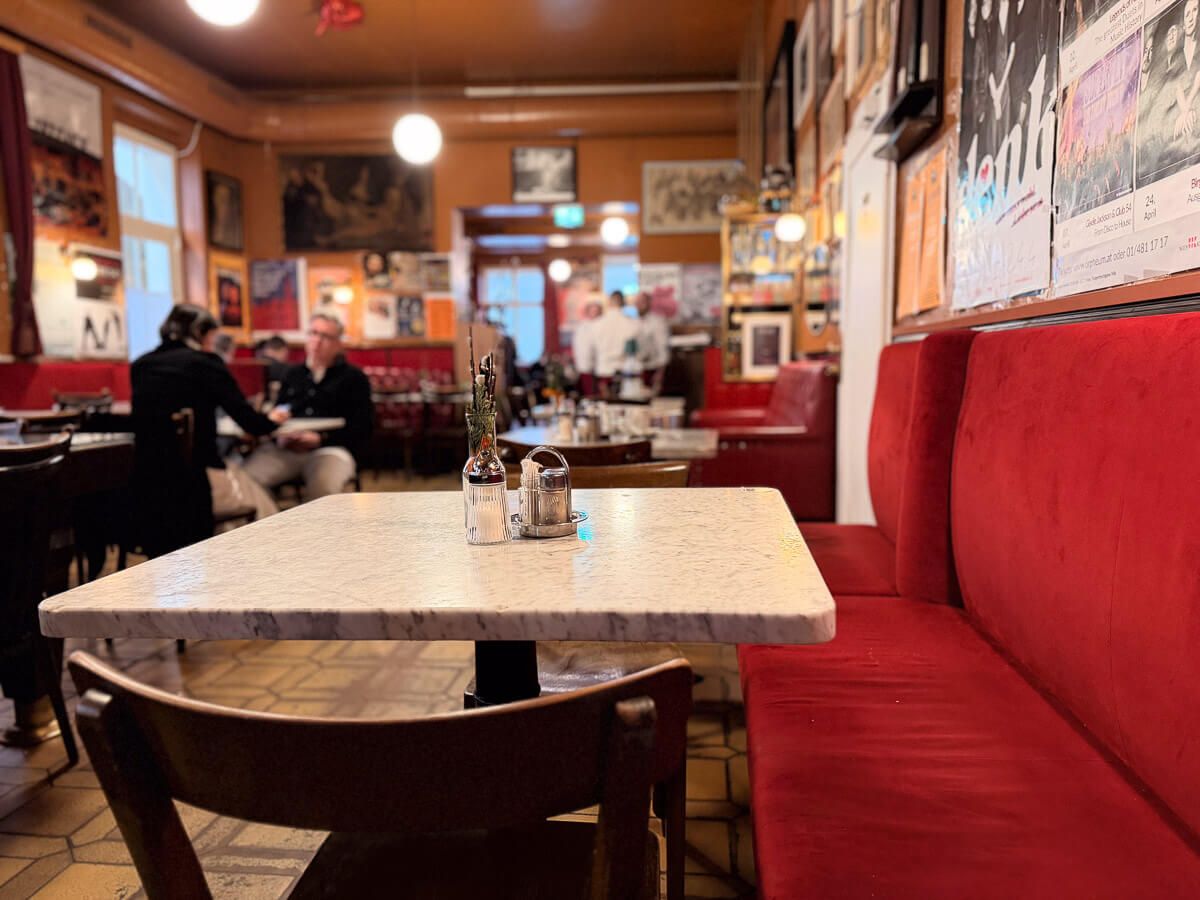 Innenraum eines Kaffeehauses mit Plakaten an den Wänden und roten Plüschsitzen