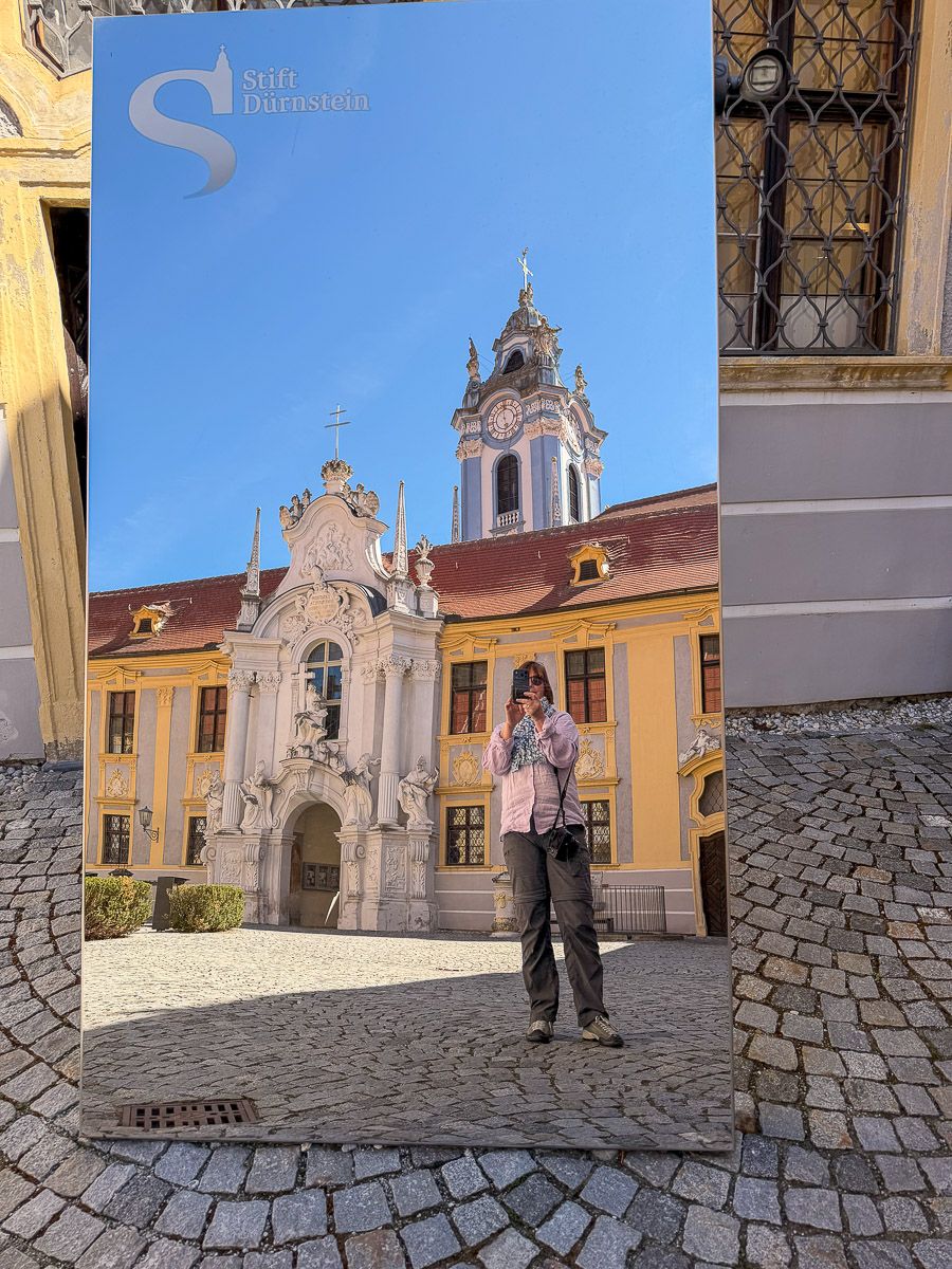 Spiegel zeigt fotografierende Frau vor dem Hintergrund des Stifts Dürnstein