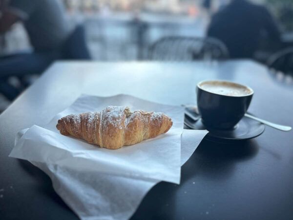 Tasse mit Kaffee und Cornetto auf einem Cafétisch