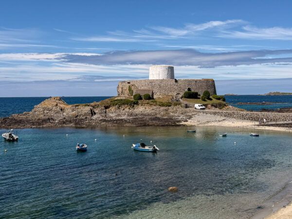Kanalinsel Guernsey: Festung and er Küste mit einem weißen Turm innerhalb der Mauern. Im Vordergrund Boote