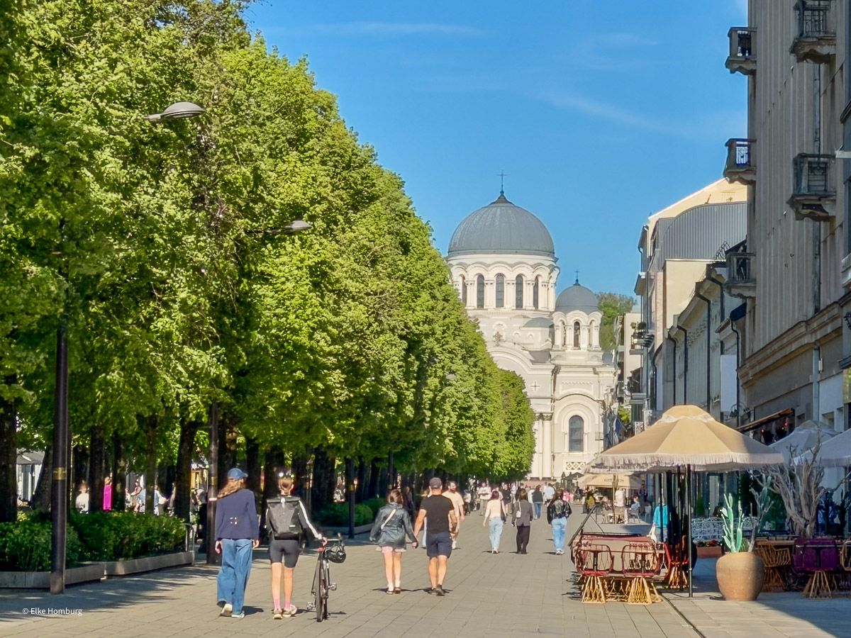 Flanierstaße mit vielen Menschen, die auf eine weiße Kirche zulaufen