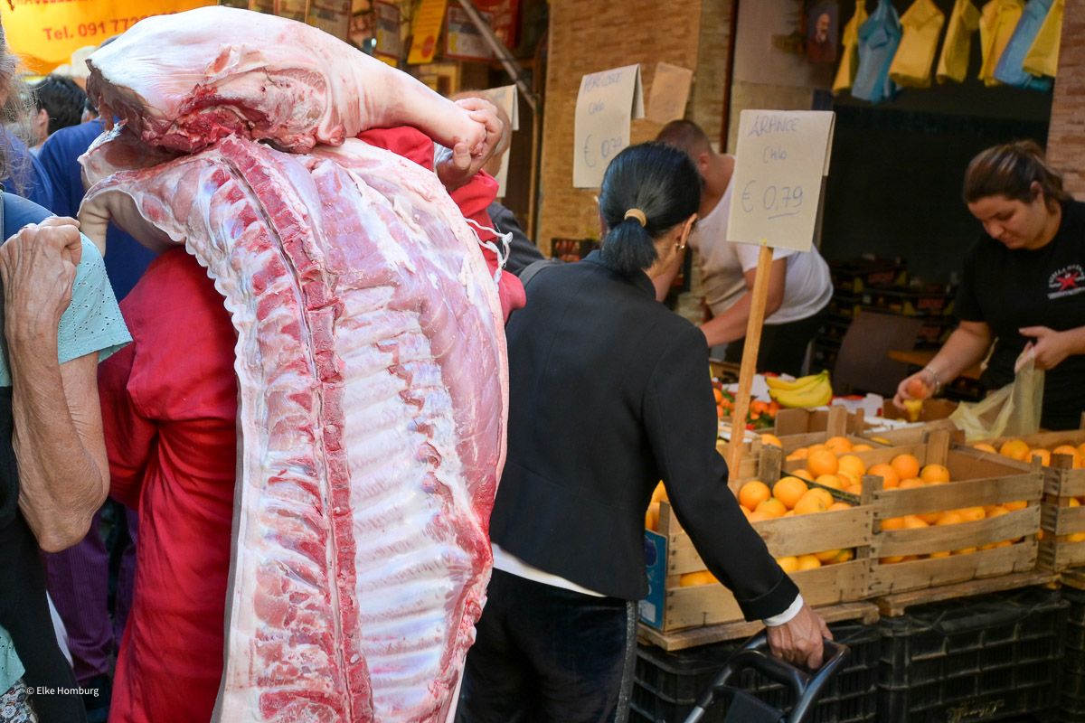 Mann trägt Schweinhälfte auf dem Rücken über den Markt 