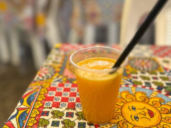 Becher mit frisch gepresstem Orangensaft auf bunter Tischdecke