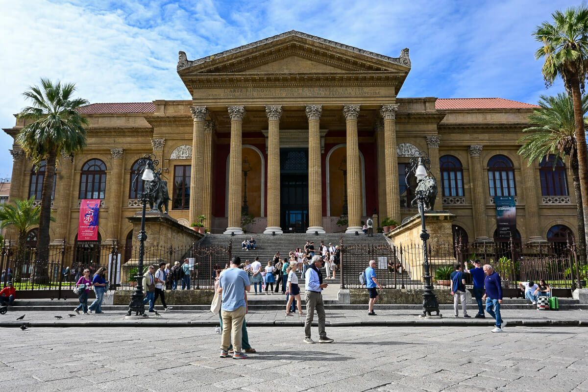 Großes Theater mit Säulenhalle, zu der Treppen führen. Davor ein belebter Platz