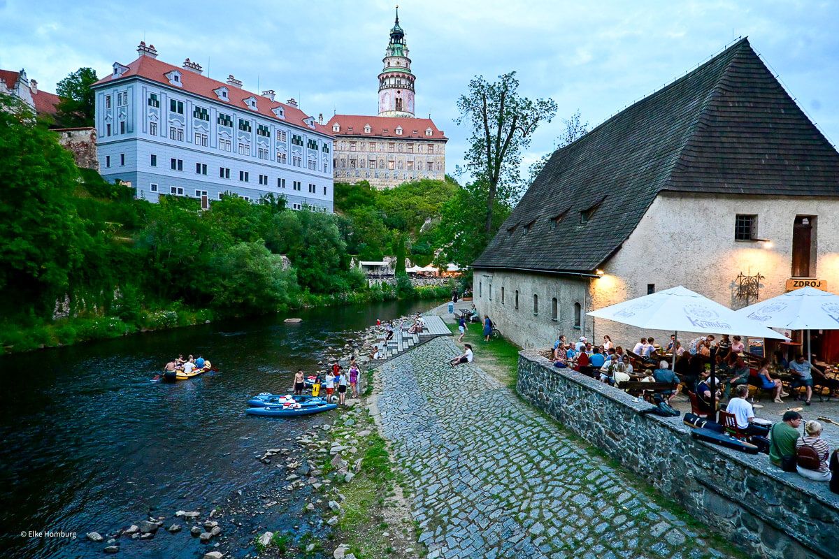 Schlauchboote treiben auf der Moldau. Links das Schloss, rechts ein Restaurant