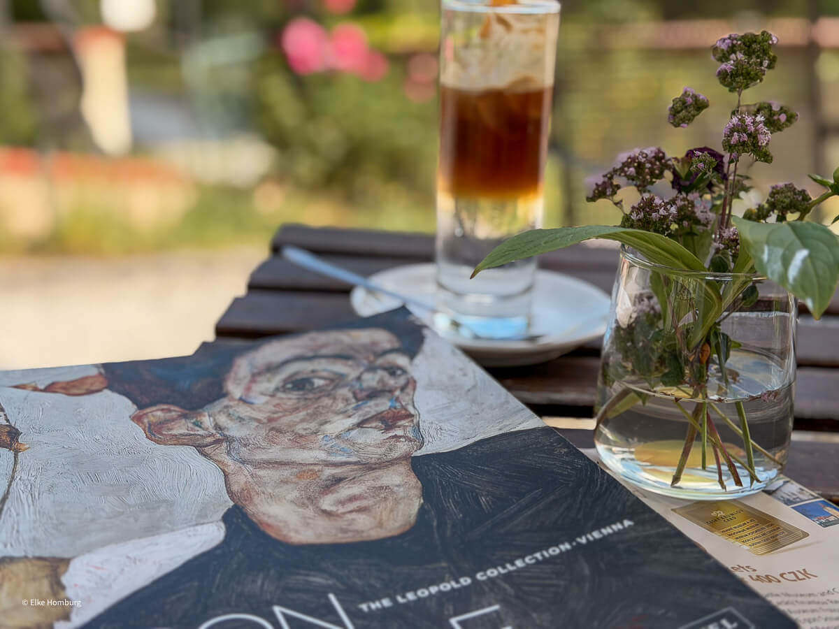 Tisch mit Blumen, Getränk und Schiele-Bildband