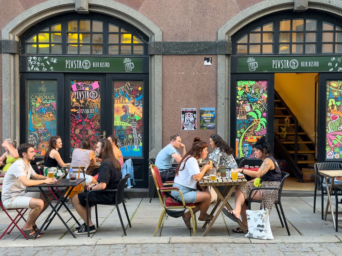 Viel mehr als eine Bierstadt: ein Wochenende in Pilsen 42 Menschen sitzen an Tischen eines bunten Lokals auf dem Gehsteig